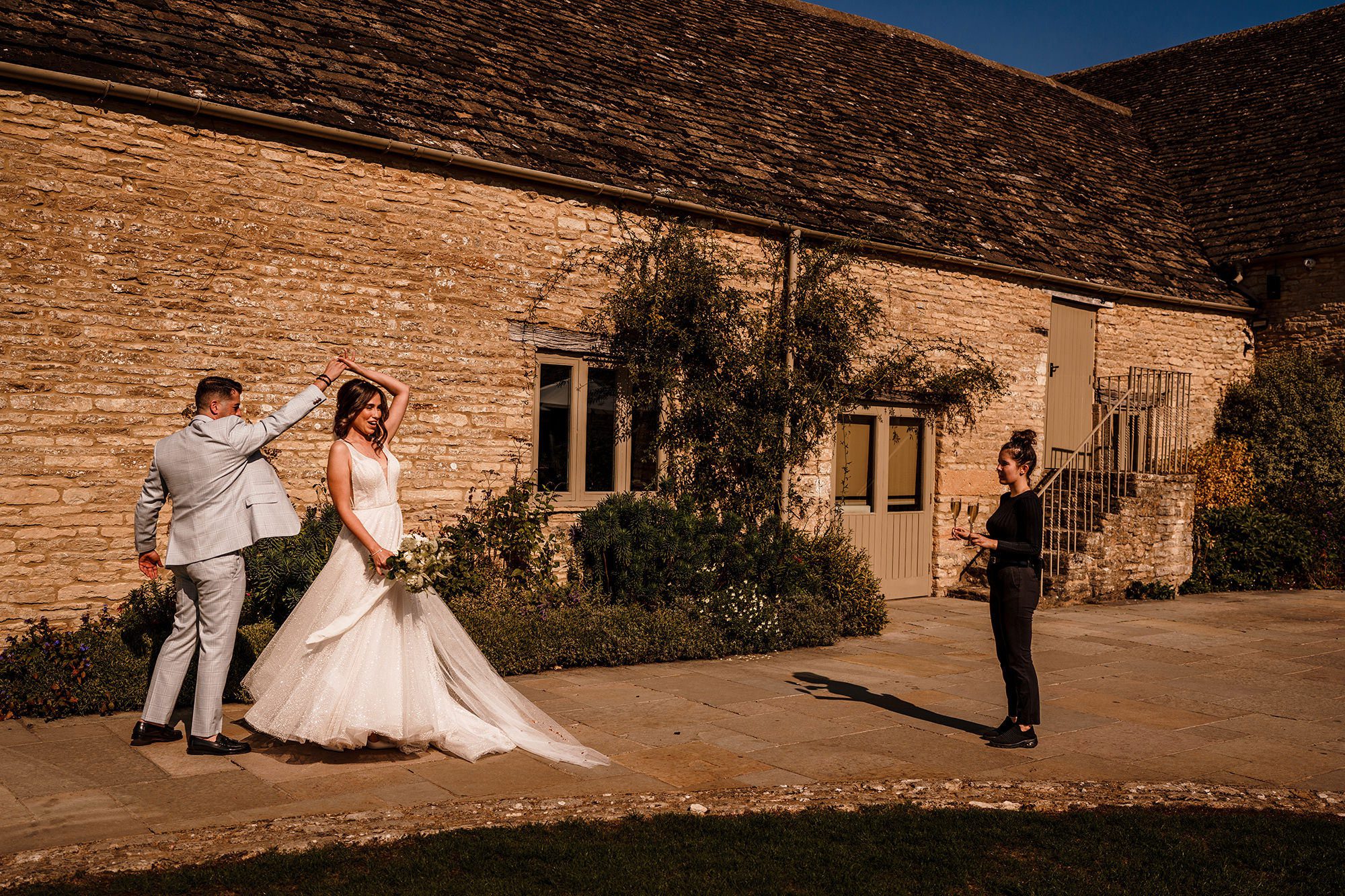 groom spins bride around with Cotswolds stone behind them