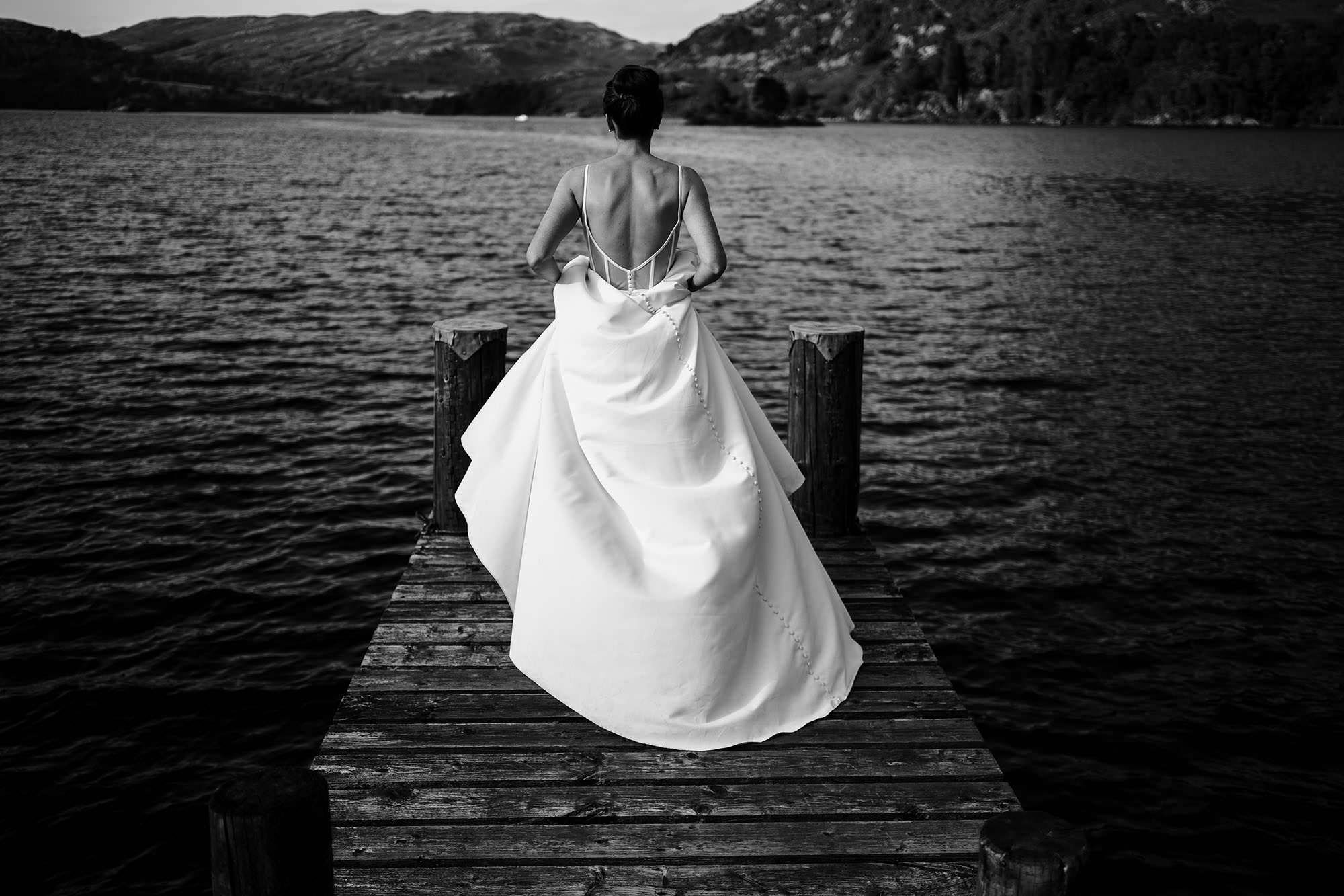 Bride in dress walks along dock in Lake District