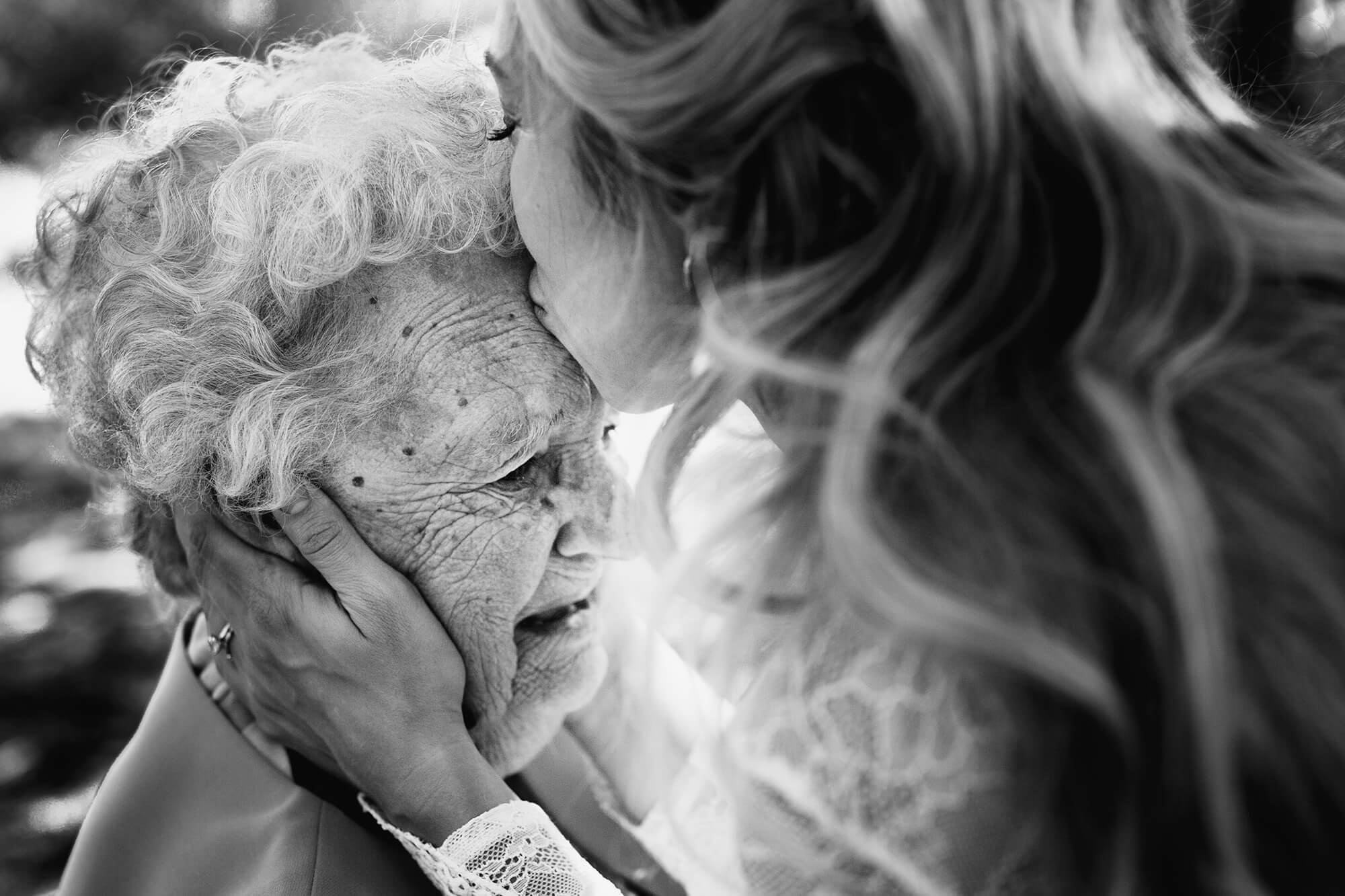 bride kisses grandma on the head for wedding photo