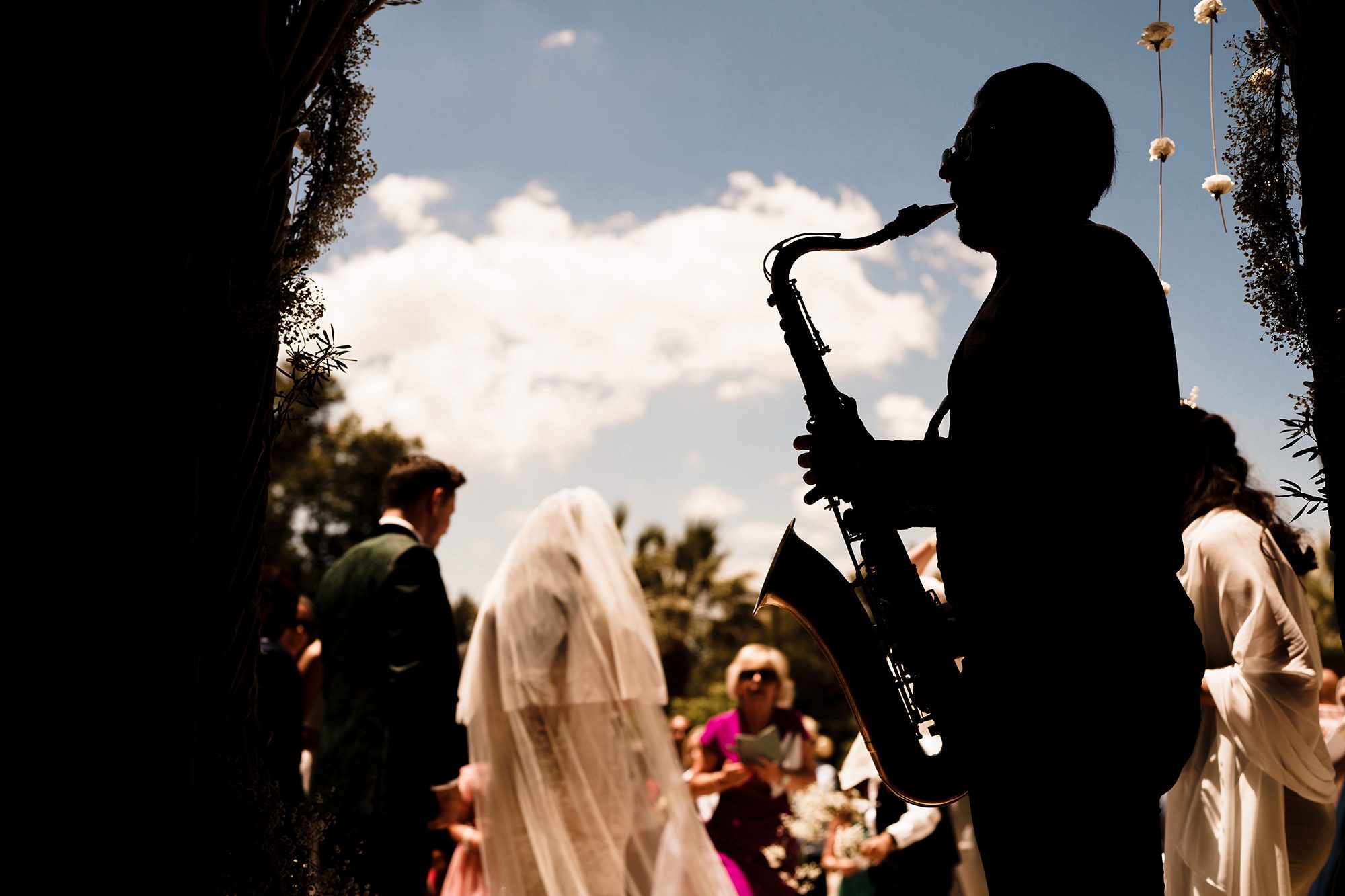 saxophonist plays in foreground with wedding guests outside in London 