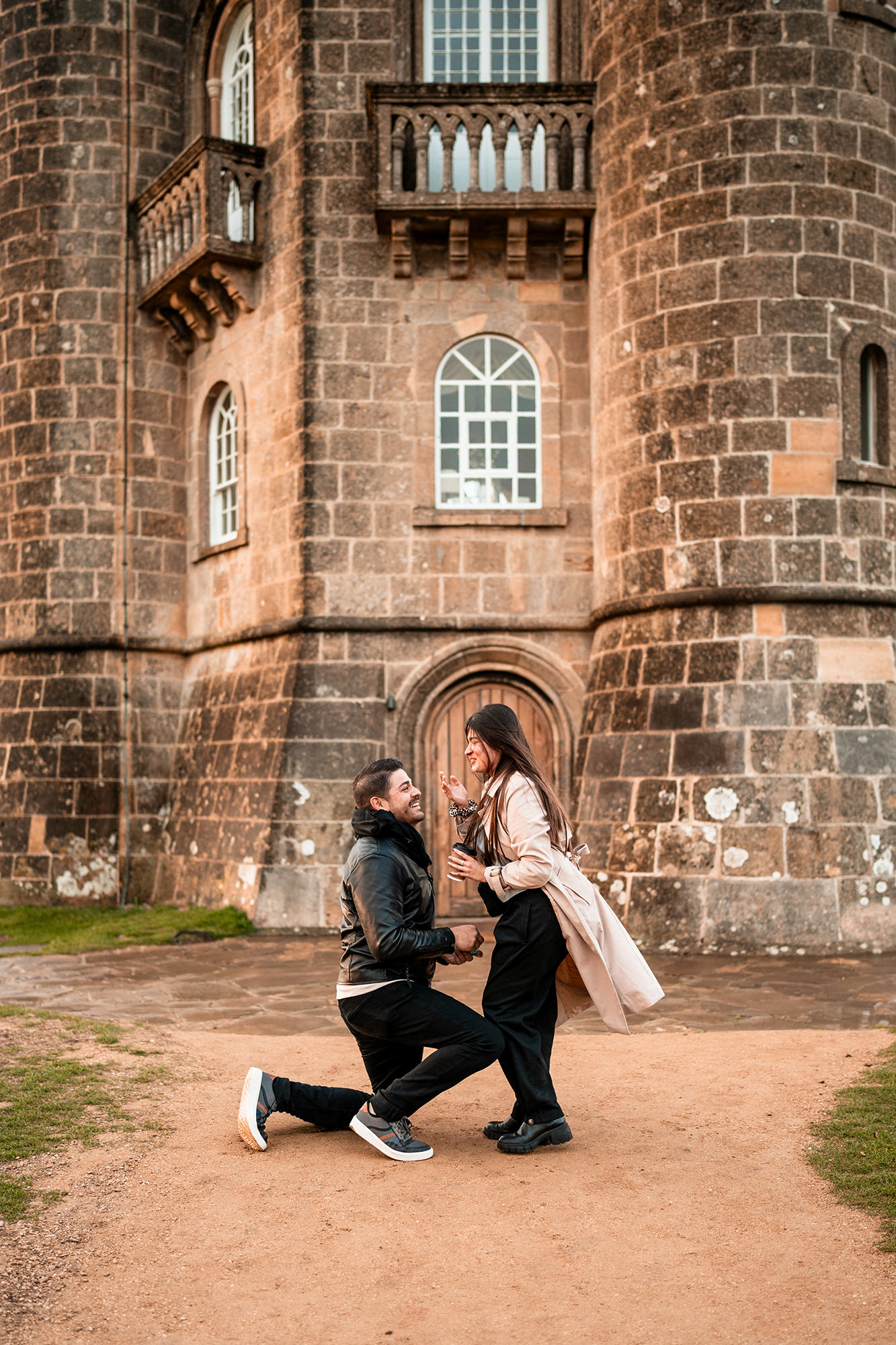 Newly engaged couple under a rainbow at Broadway Tower in the Cotswolds