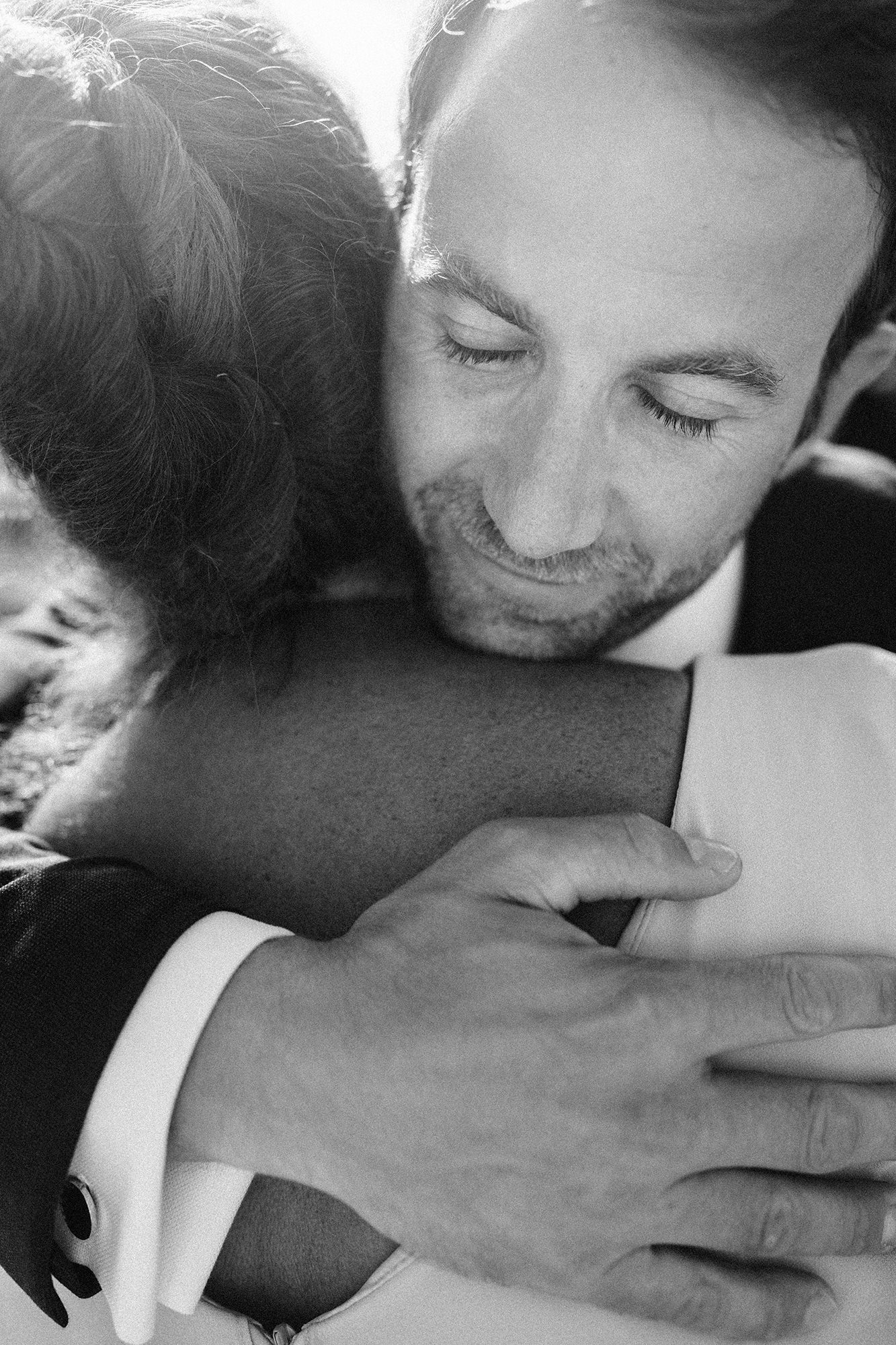 Emotional black and white candid photograph of a groom hugging a guest