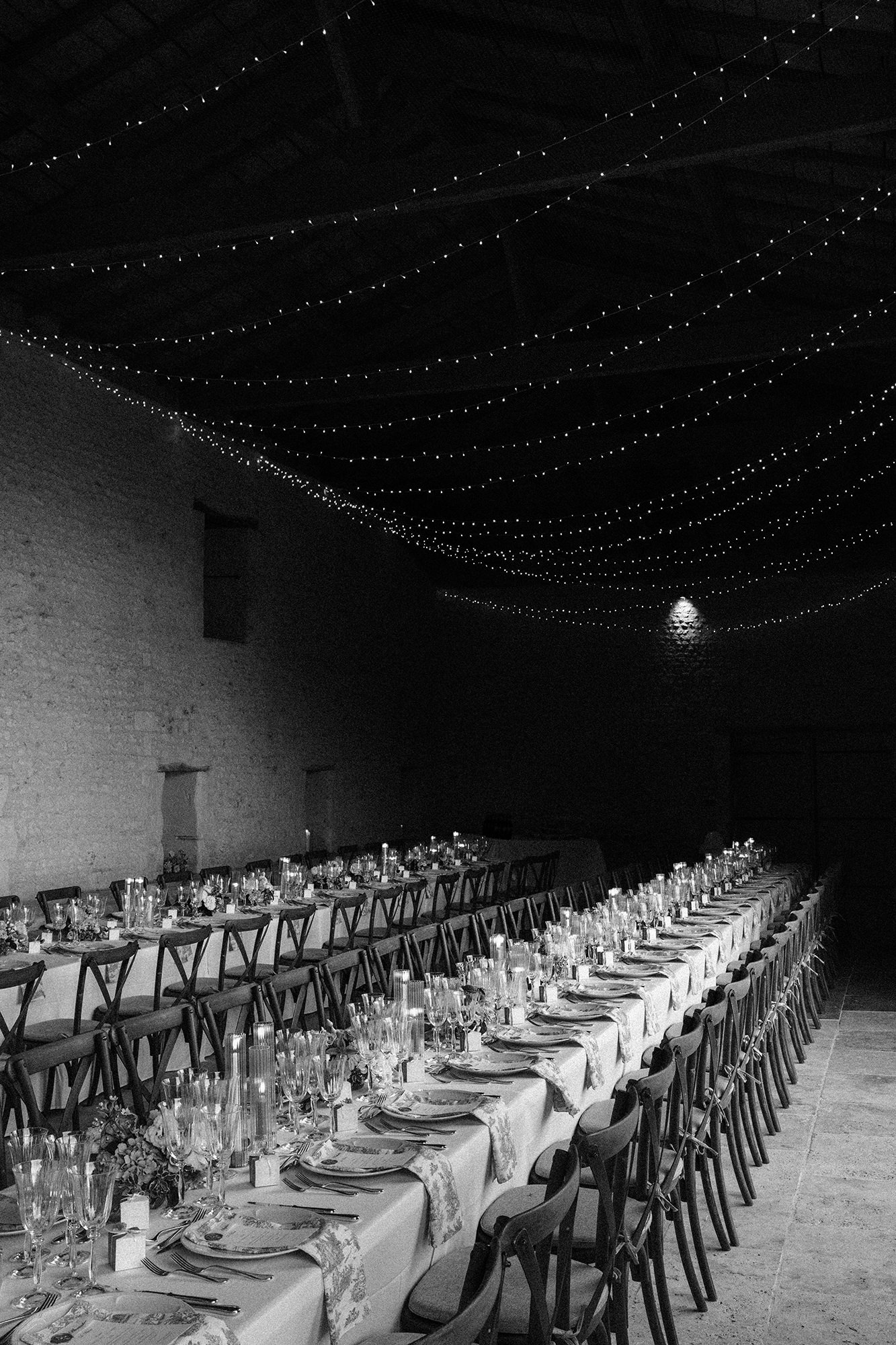Long wedding breakfast tables beneath fairy lights at a French wedding