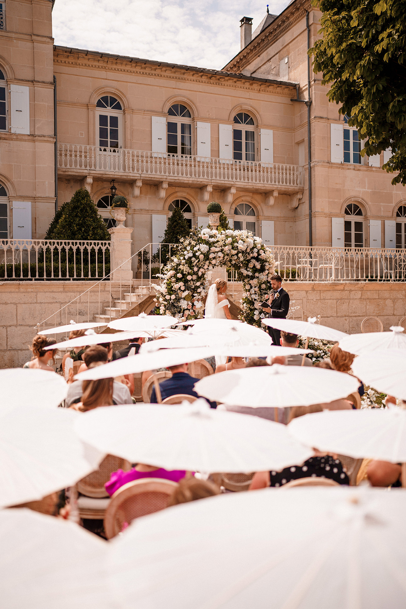 Outdoor château wedding ceremony with guests beneath white parasols