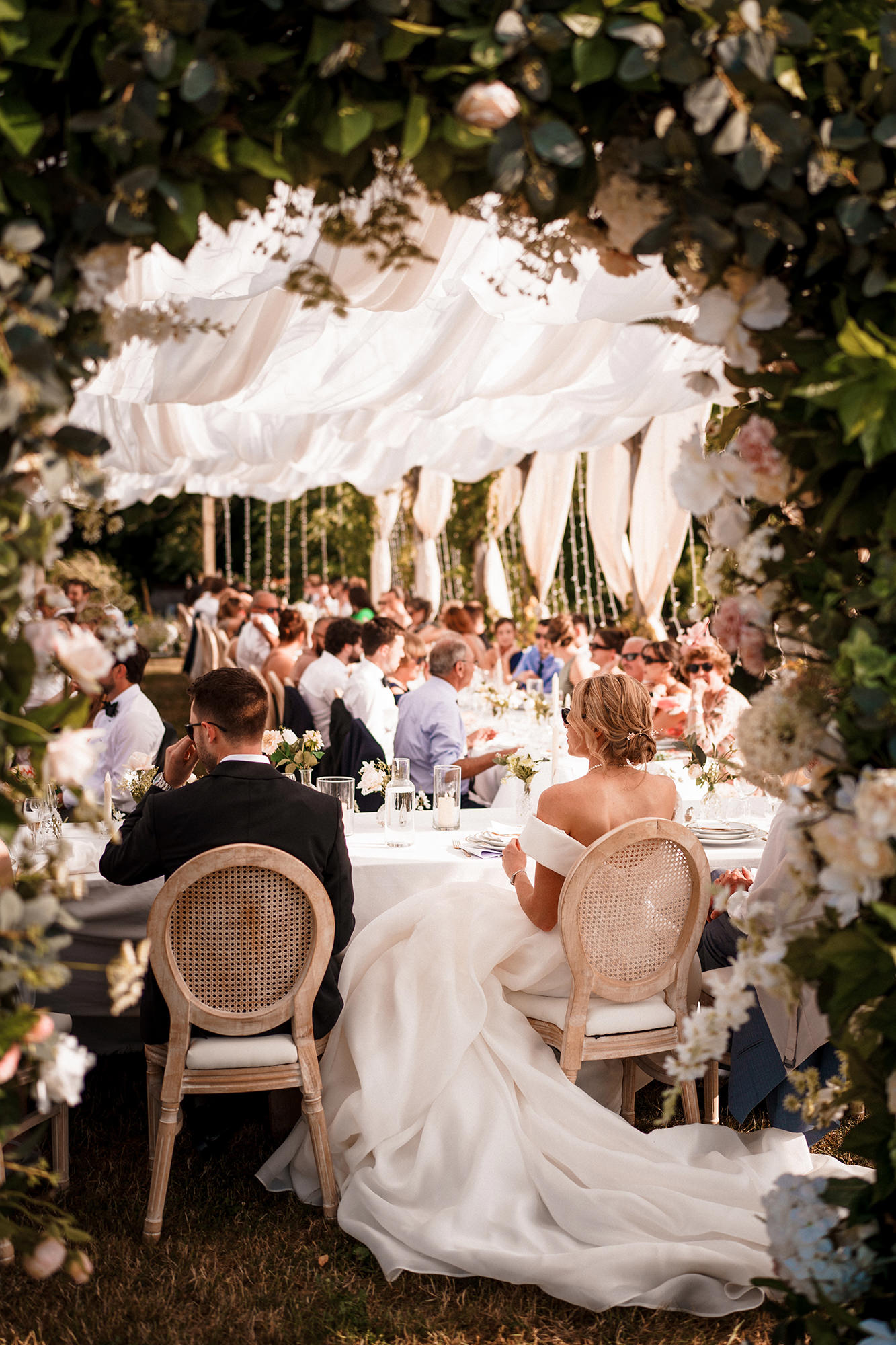 Bride and groom seated amongst guests at an outdoor wedding breakfast in France