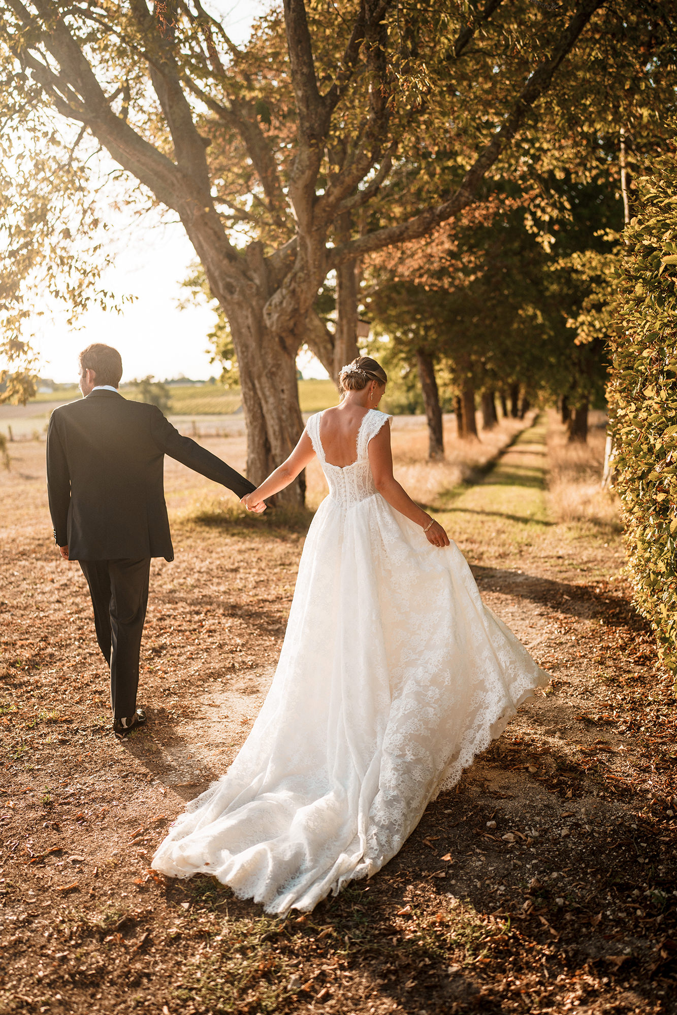 Bride and groom walking along a tree-lined path in golden evening light