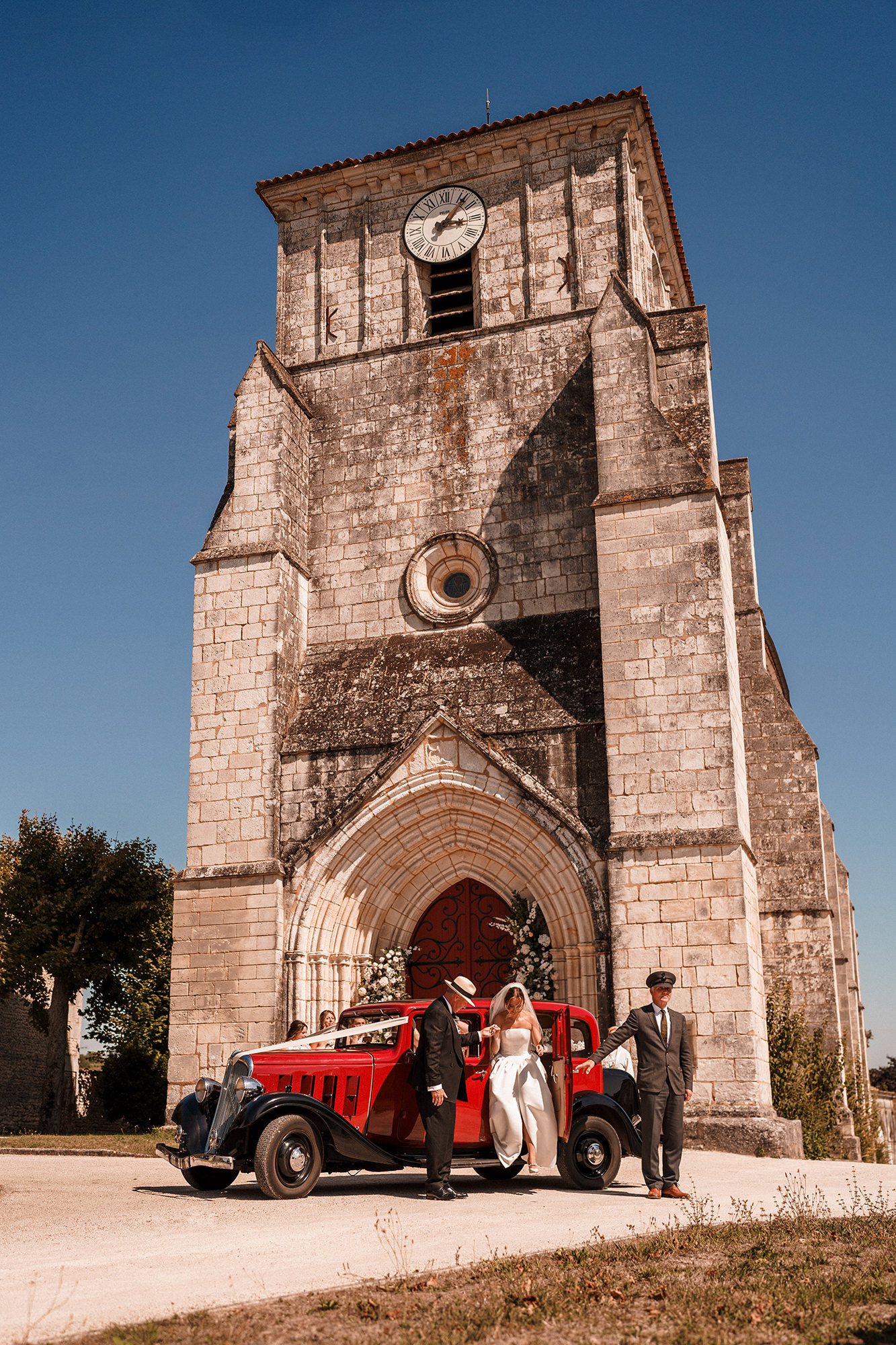 Bride and groom arriving beside a vintage car outside a church in France